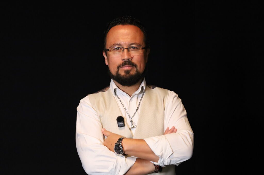Óscar Avendaño, experto en LinkedIn en Colombia, con los brazos cruzados sobre fondo oscuro, para optimizar tu perfil de LinkedIn